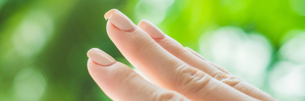 有丙烯酸指甲的女士手。中指指甲有裂纹或缺口。