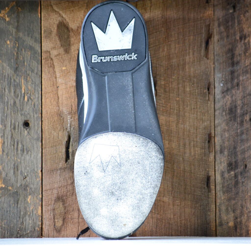 黑色和灰色的布伦瑞克保龄球鞋与橡胶鞋底和肮脏的保龄球鞋滑梯影响保龄球手的比赛。建议清洗保龄球鞋。
